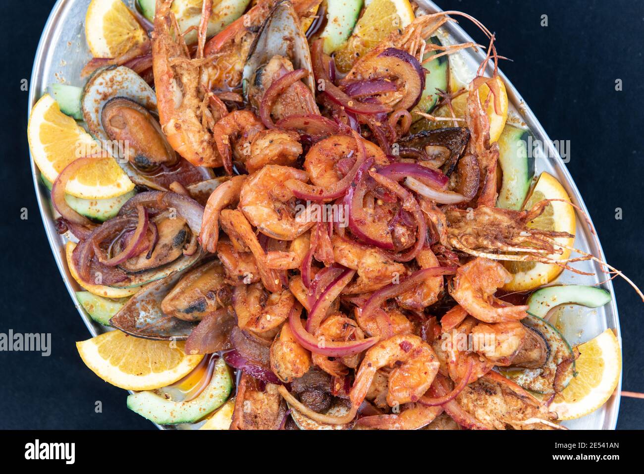 Overhead view of large pile of spicy shrimp plate served over roasted vegetables and garnished with orange slices. Stock Photo