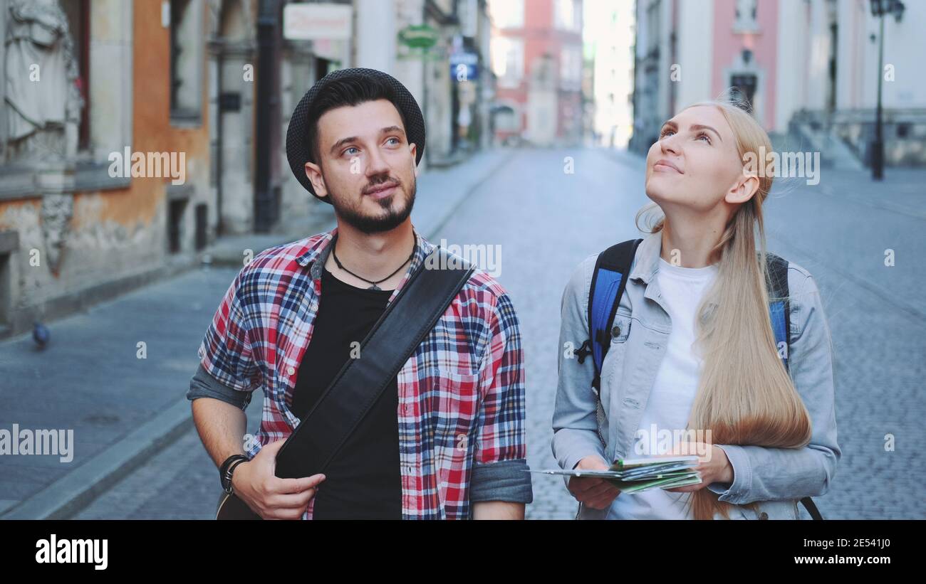 Happy young tourist couple with map walking and looking at old city architecture. Sightseeing in beautiful european city. Stock Photo