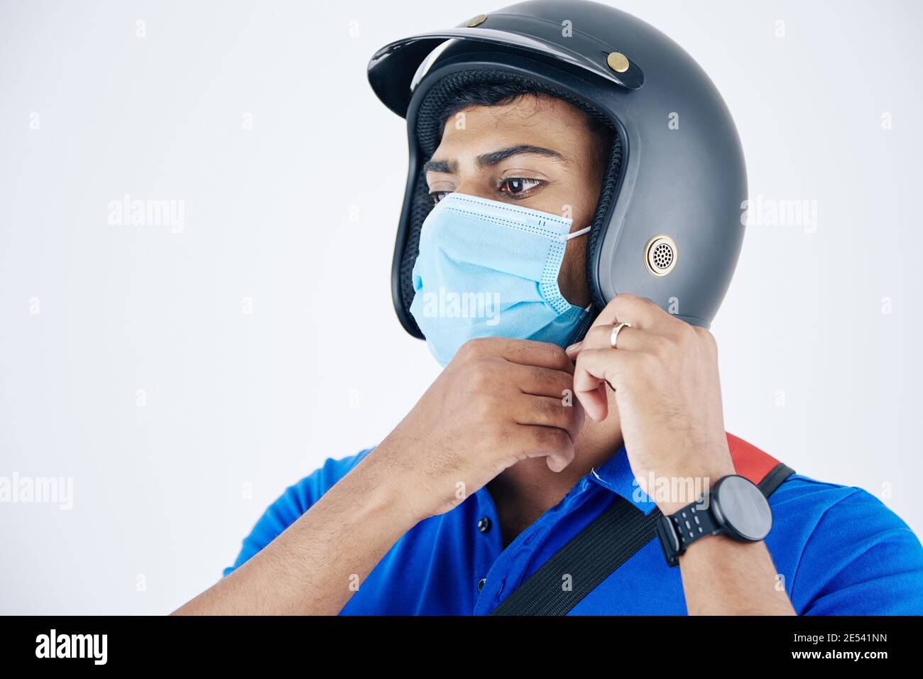 Young serious Indian courier in protective mask fastening helment and getting ready to deliver foot to customer Stock Photo