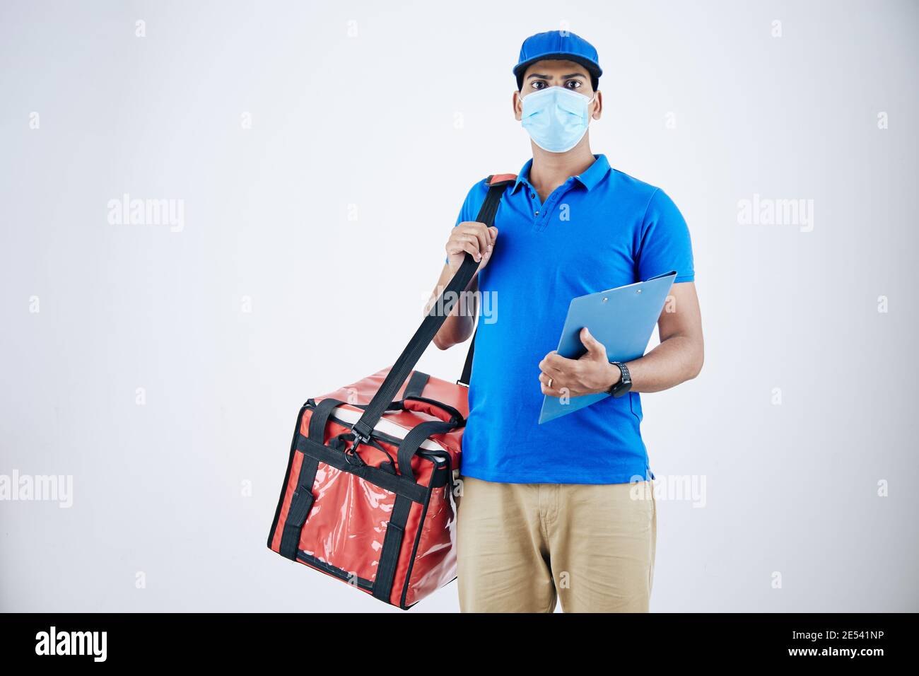 Young Indian courier in medical mask deliverying food in cooler bag, isolated on white Stock Photo
