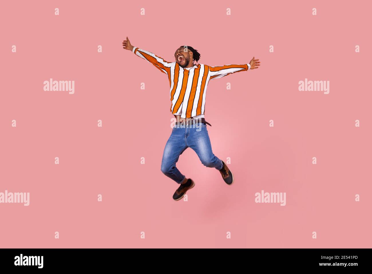 Extremely happy excited afro-american man with dreadlocks in striped shirt highly jumping widely opening hands and screaming feeling freedom. Indoor s Stock Photo