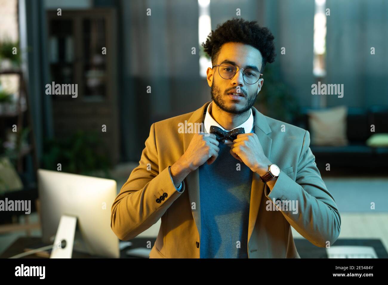 Portrait of young man in eyeglasses looking at camera wearing bow tie to his stylish suit while standing at office Stock Photo