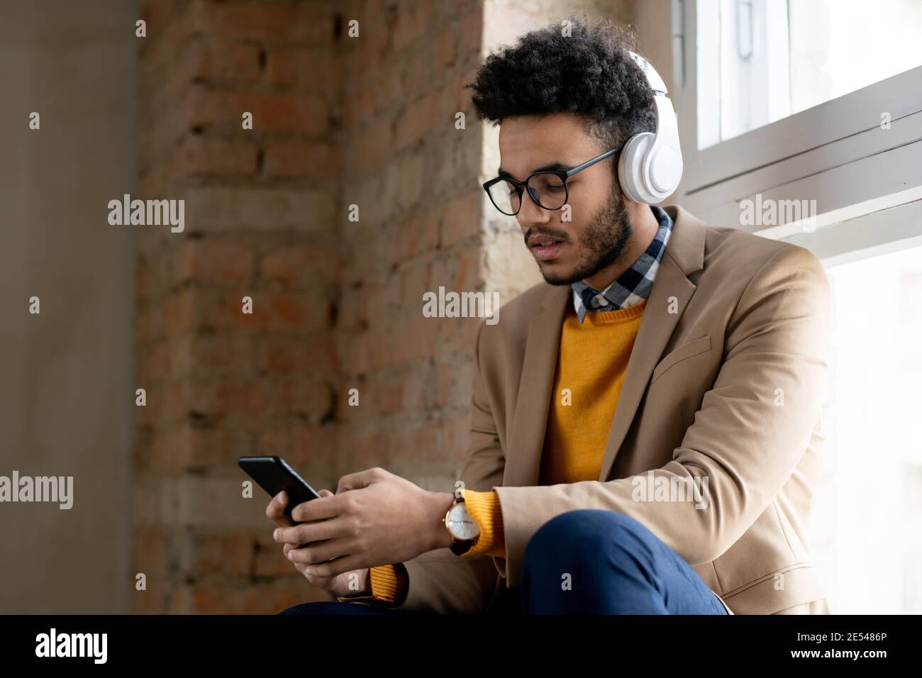 Young man in wireless headphone using his mobile phone to listen to music Stock Photo