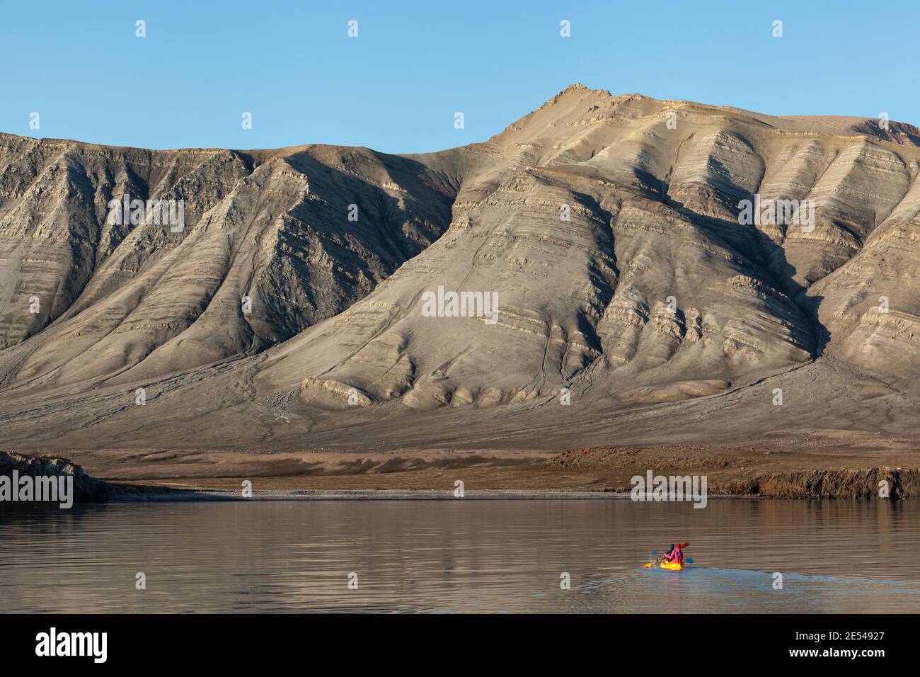 A person in a orange kayak paddling towards mountains in Baffin Bay Stock Photo