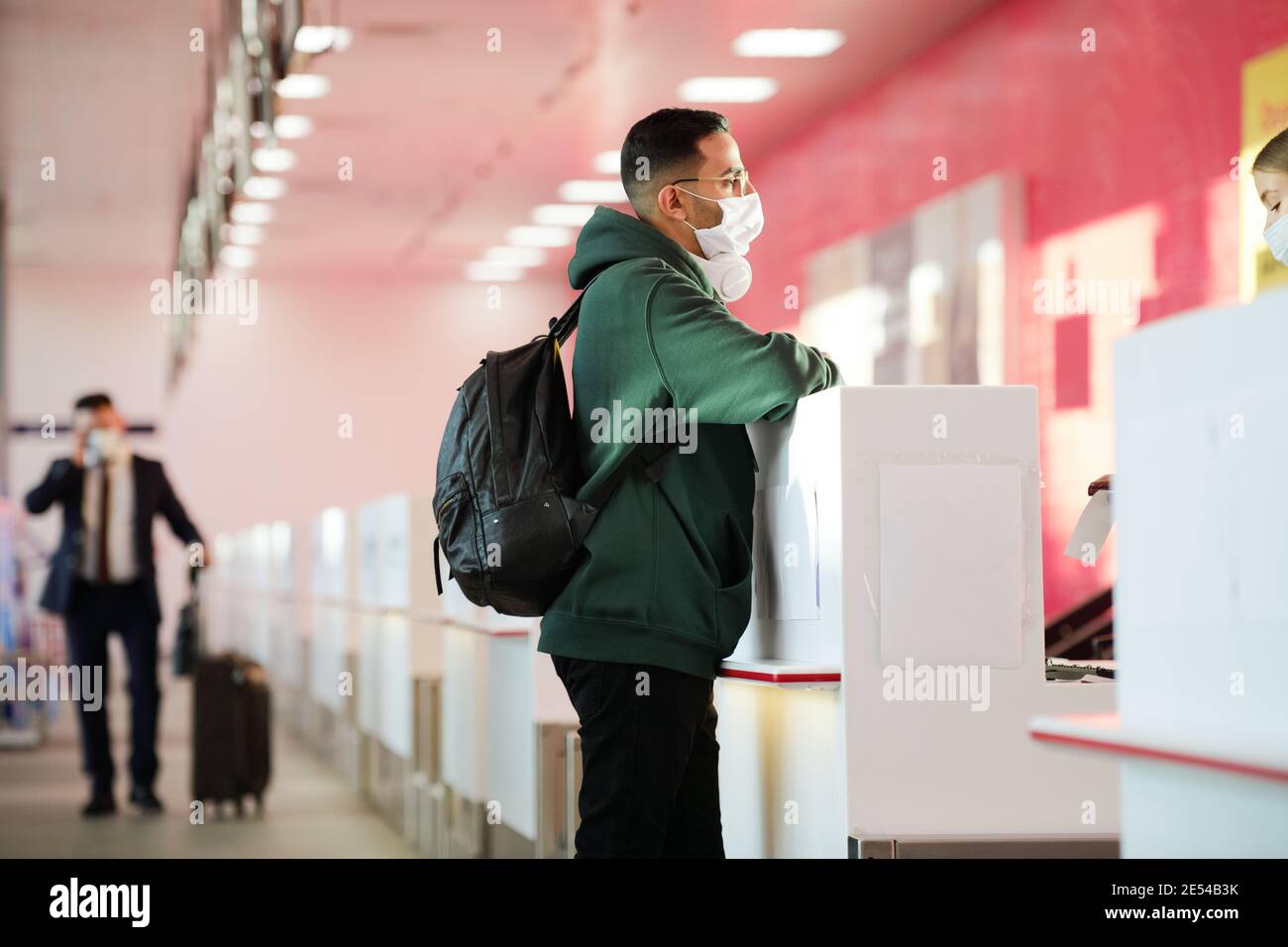Man in protective mask with backpack behind his back standing at reception desk at the airport Stock Photo