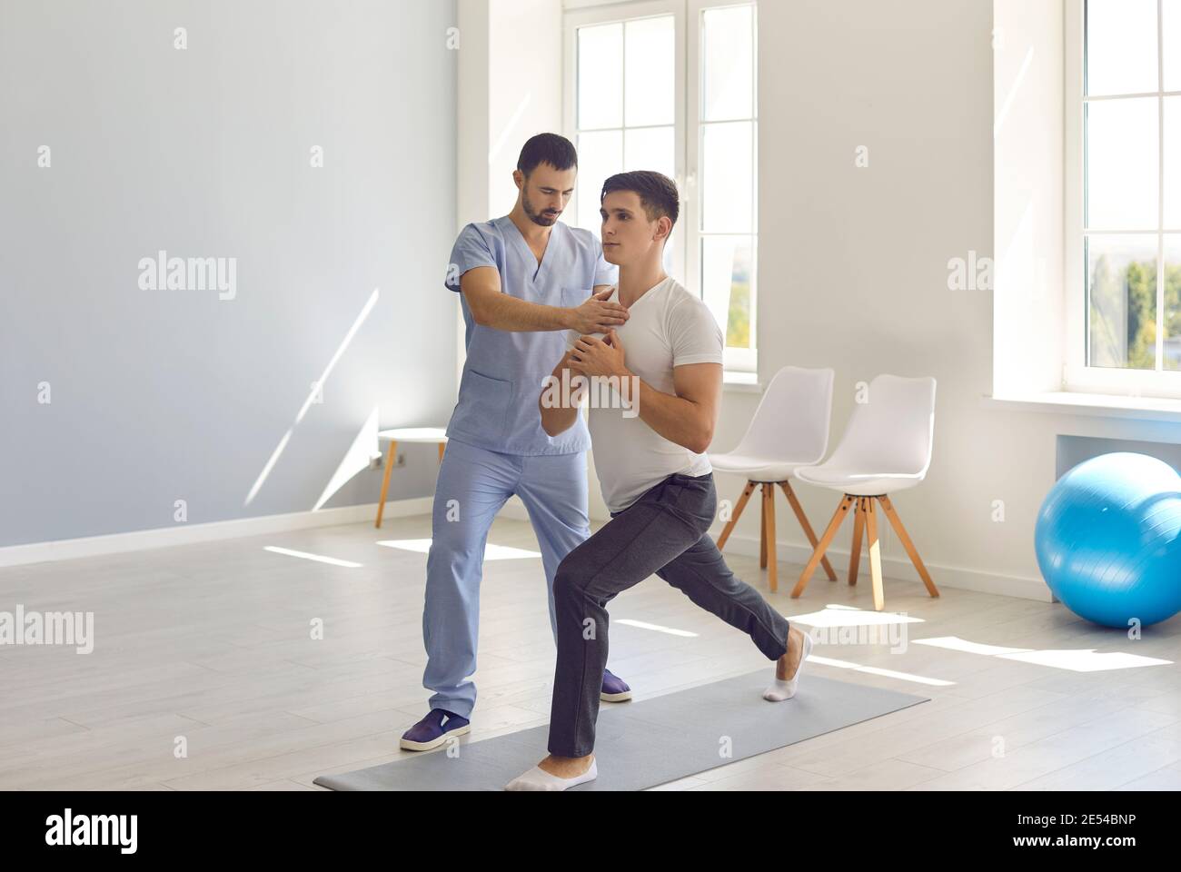 Osteopath fixing and controlling man patients movements during exercising on fitness mat Stock Photo