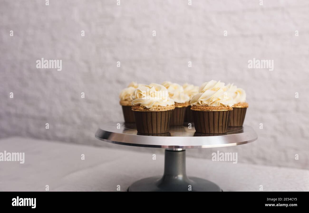 the chef girl sprinkles icing on fresh cupcakes covered in vanilla cream.Sweet homemade cupcakes with cream on a tray. Food for breakfast. Freshly Stock Photo