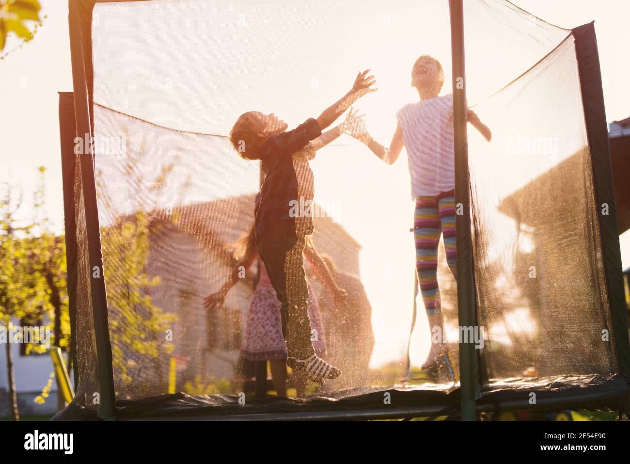 Cheerful happy kids having fun and jumping in a trampoline on a sunny ...
