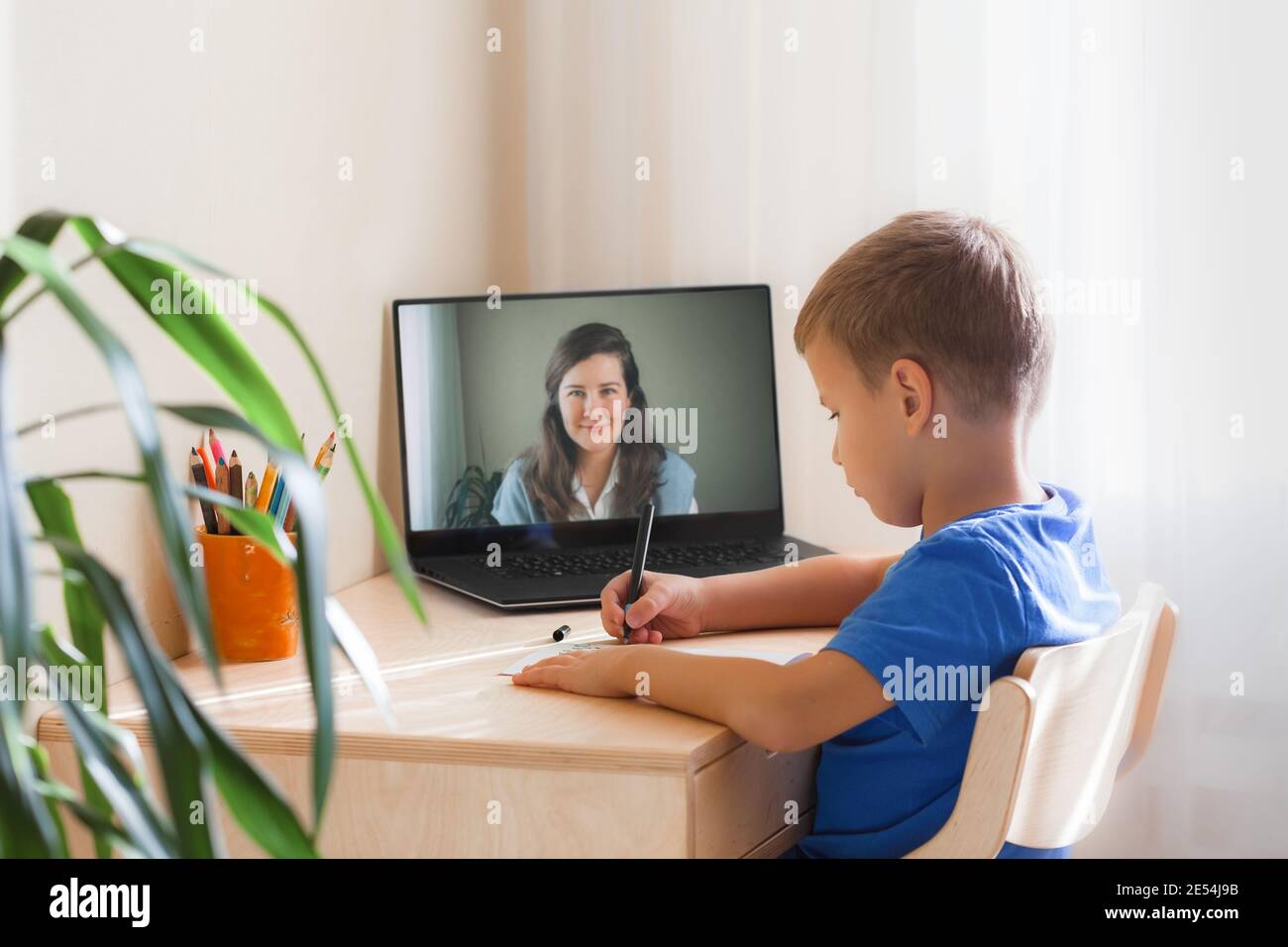 7 years old boy sitting by desk with laptop doing writing task during