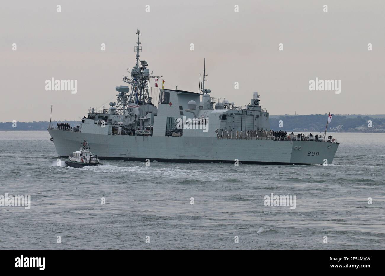 The Royal Canadian Navy frigate HMCS HALIFAX (FFH330) is escorted by a pilot vessel as it turns and heads into The Solent Stock Photo