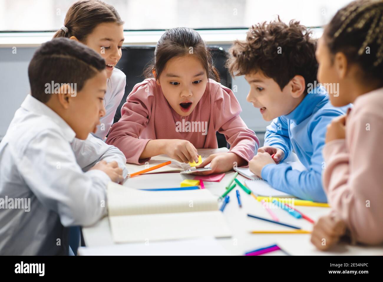 Diverse small schoolchildren using phone at classroom Stock Photo