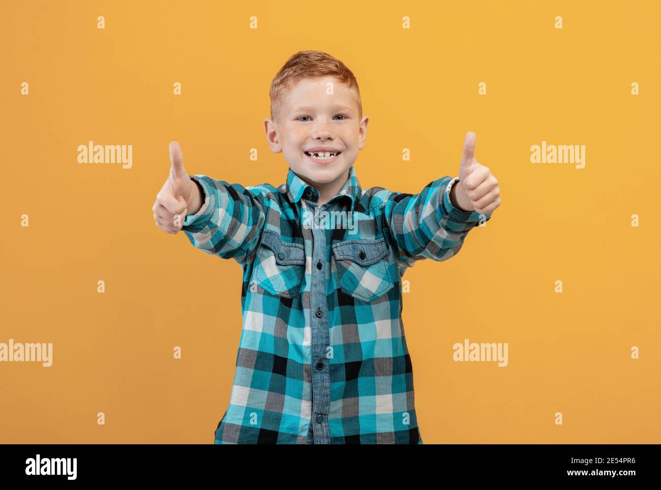 Happy ginger kid showing thumbs up on yellow studio background Stock Photo