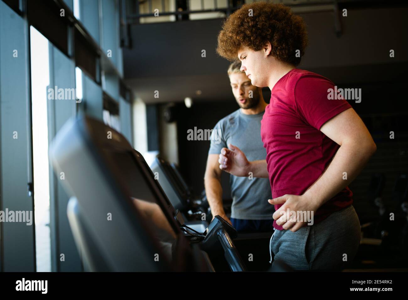 Overweight young man with trainer exercising in gym Stock Photo