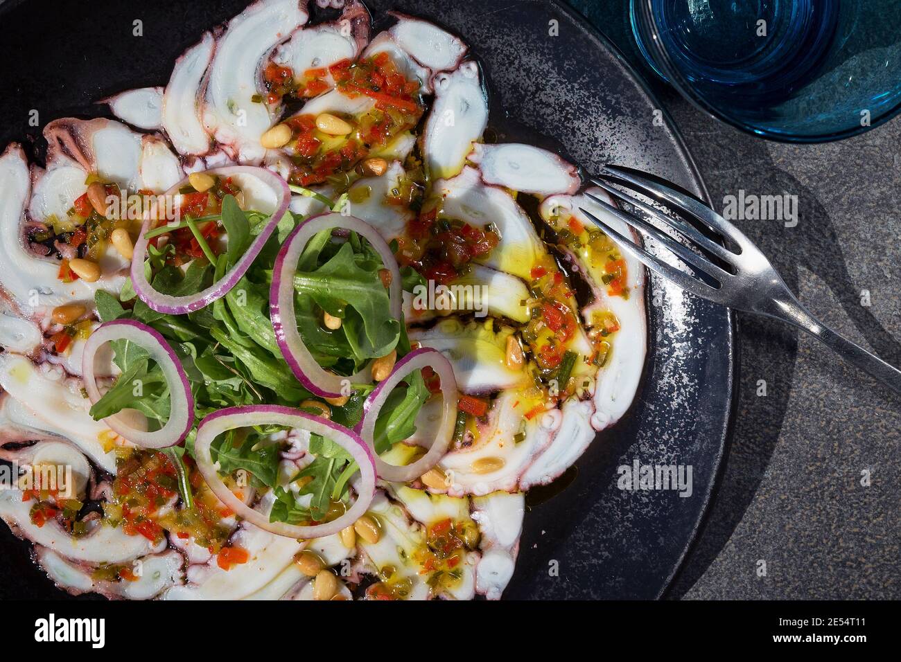 Close up gray dish of octopus carpaccio with onion and rocket salad Stock Photo