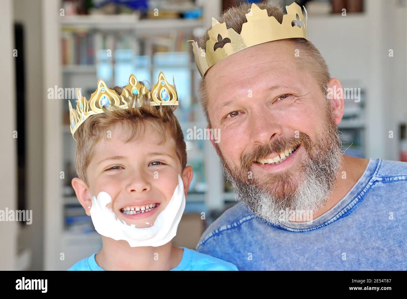 Father and son put the crown on their heads and have fun. Father has a beard. Son made a beard out of shaving foam Stock Photo