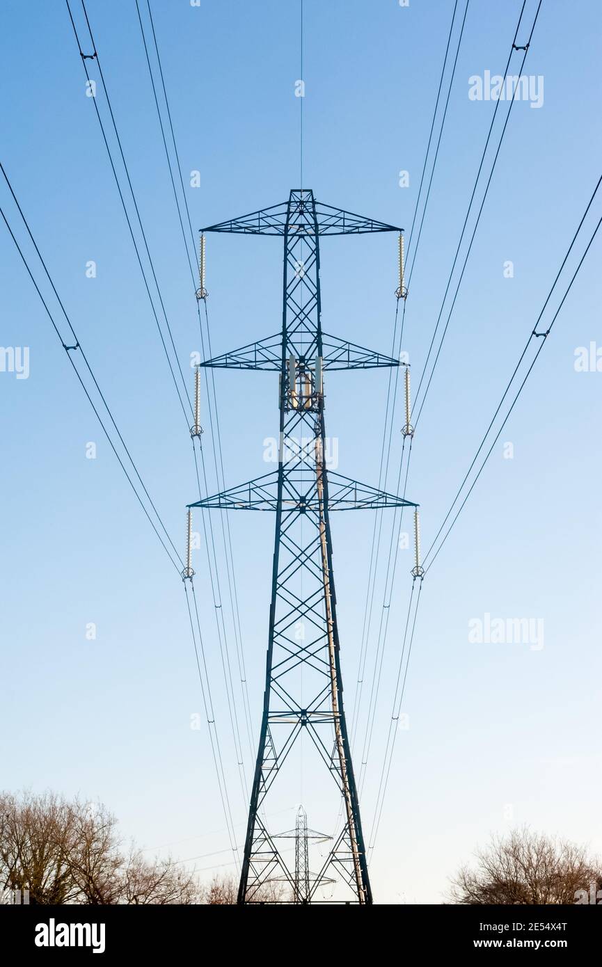 high voltage electric power lines in early morning sunlight against a blue sky Stock Photo