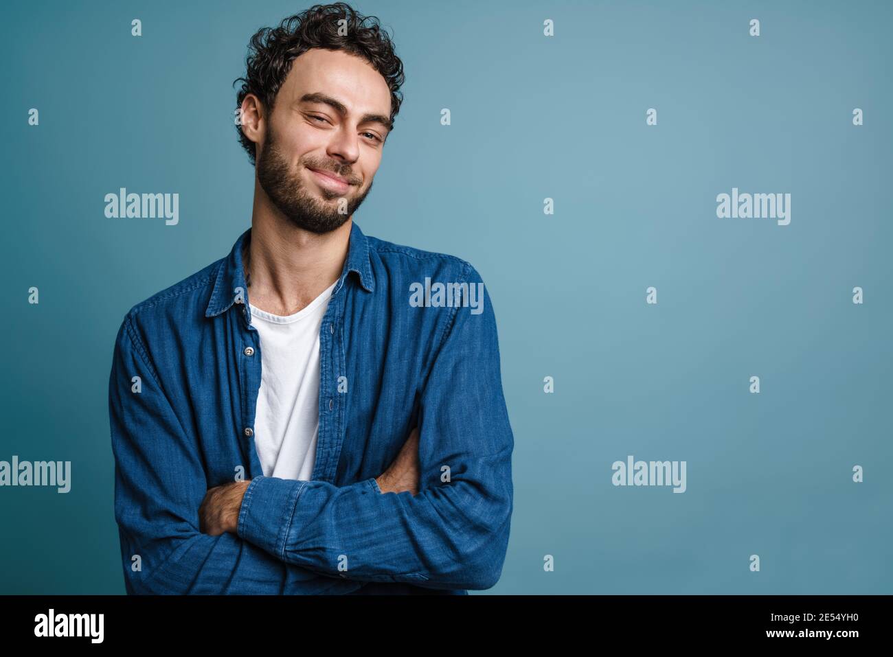 Joyful handsome guy smiling and while posing with hands crossed isolated over blue background Stock Photo