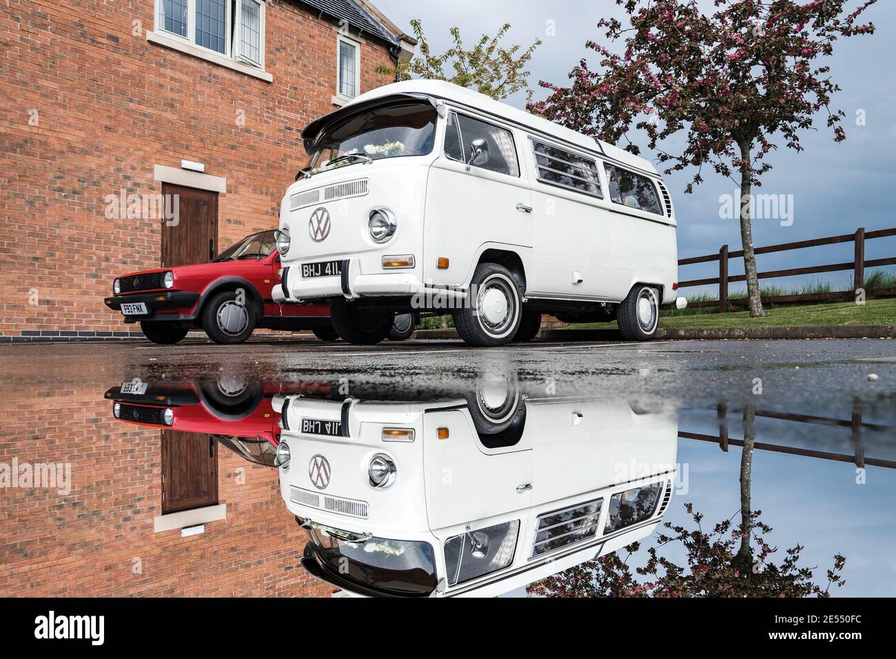 VW camper van reflection in puddle after rain white water cooled screen classic Volkswagen wedding car cream steel wheels red Polo Golf mirror image Stock Photo