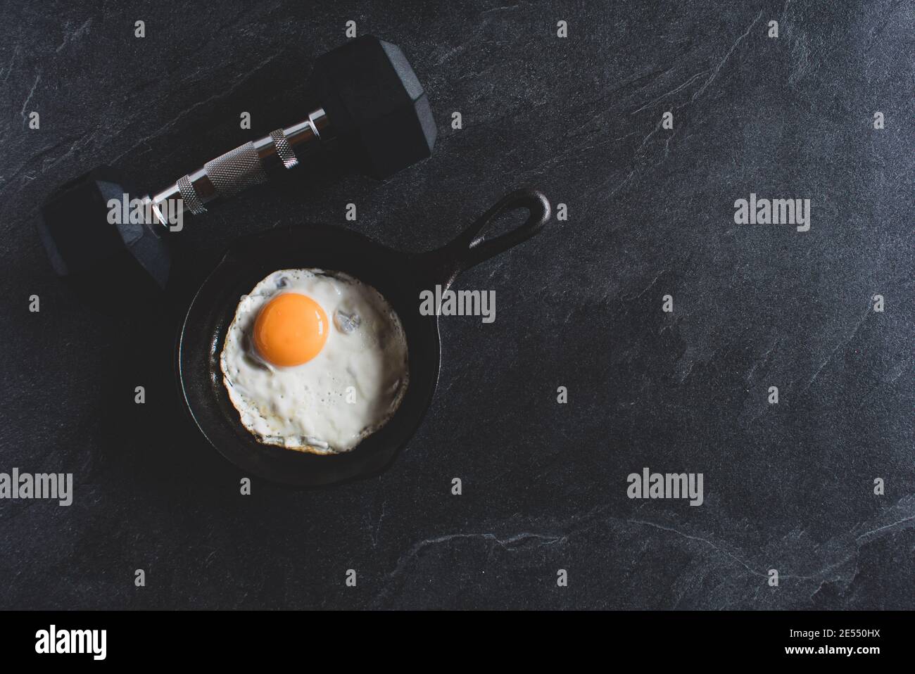 dumbbell with pan fried egg on dark background from above with copy space Stock Photo