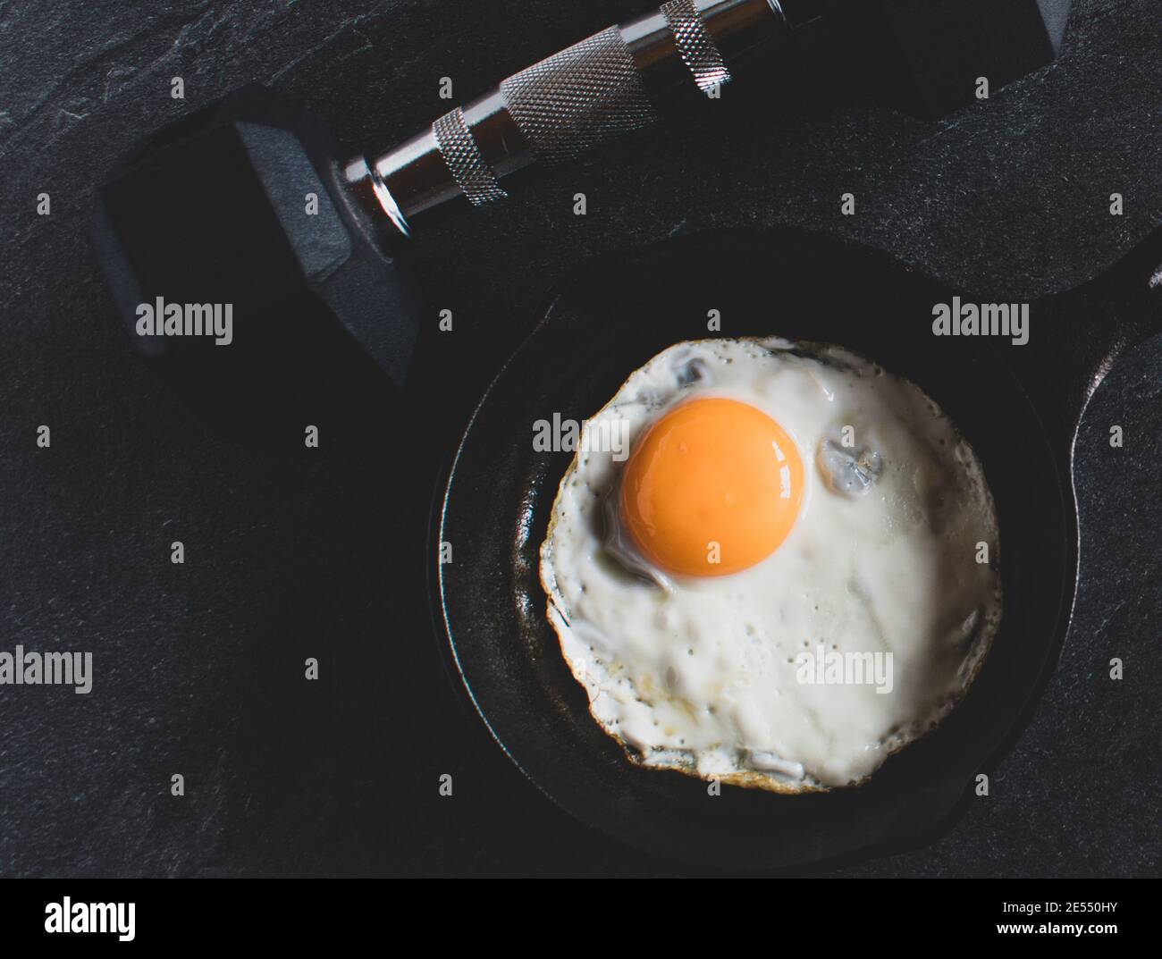 dumbbell with pan fried egg in a pan on dark bakground from above Stock Photo