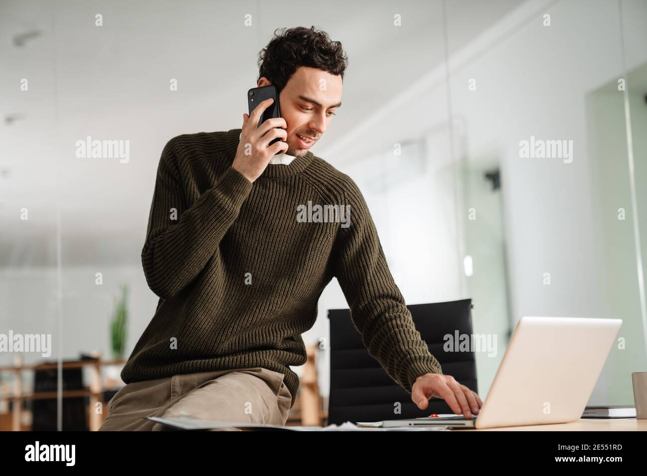 Confident young manager working at the office, holding documents, using laptop computer Stock Photo