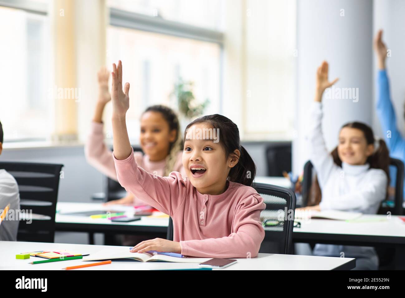 Diverse small schoolchildren raising hands at classroom Stock Photo