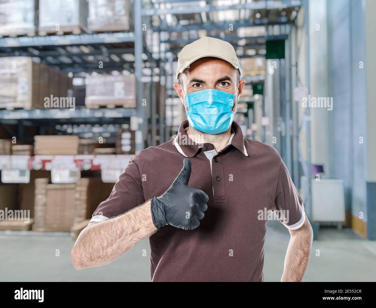 delivery man with uniform and protective mask for covid-19 inside a warehouse. Safe shipping concept. Stock Photo