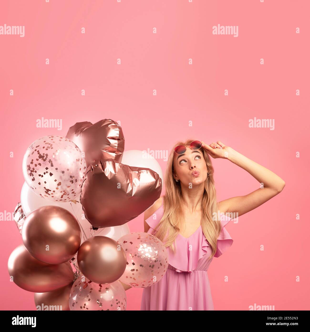 Holiday sale concept. Cute blonde woman holding bunch of balloons, pursing her lips and looking upwards at copy space Stock Photo