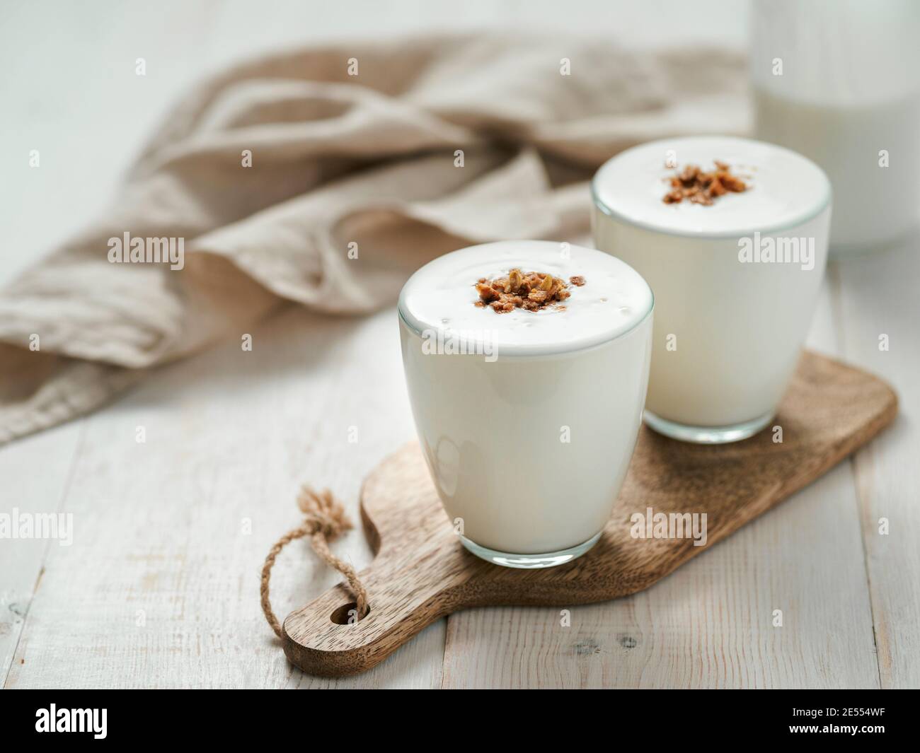 Kefir, buttermilk or yogurt with granola. Yogurt in glass on white wooden background. Probiotic cold fermented dairy drink. Gut health, fermented products, healthy gut flora concept. Copy space Stock Photo