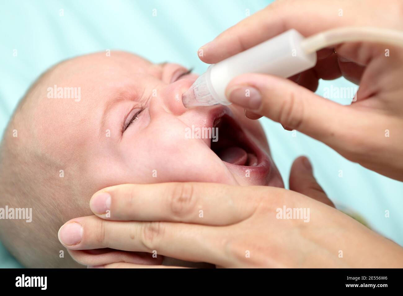 Mother cleaning mucus catarrh of baby nose with a nasal aspirator Stock Photo