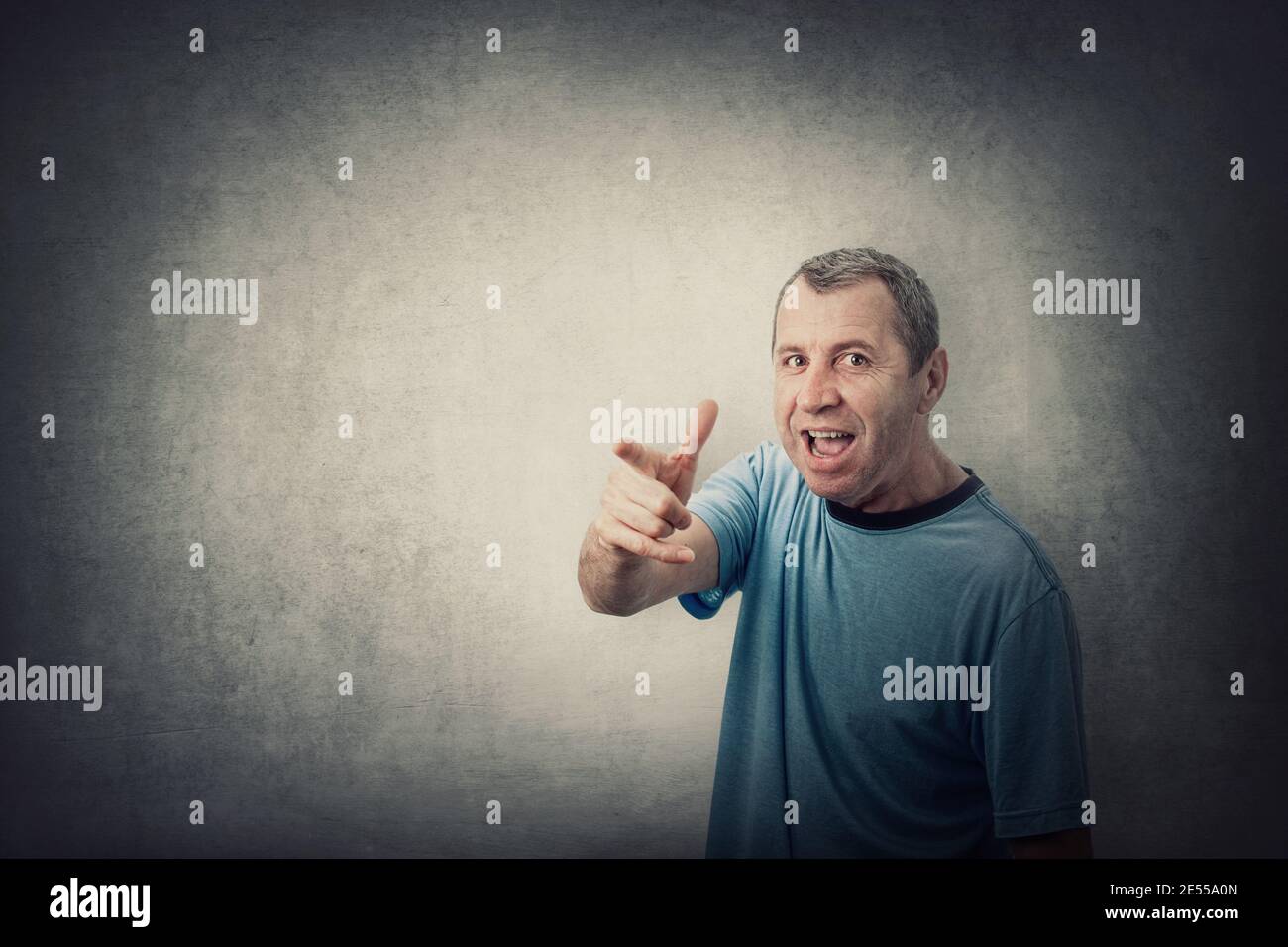 Angry middle aged man pointing index finger screaming, like scolding someone, isolated on grey wall background with copy space. Irritated and annoyed Stock Photo