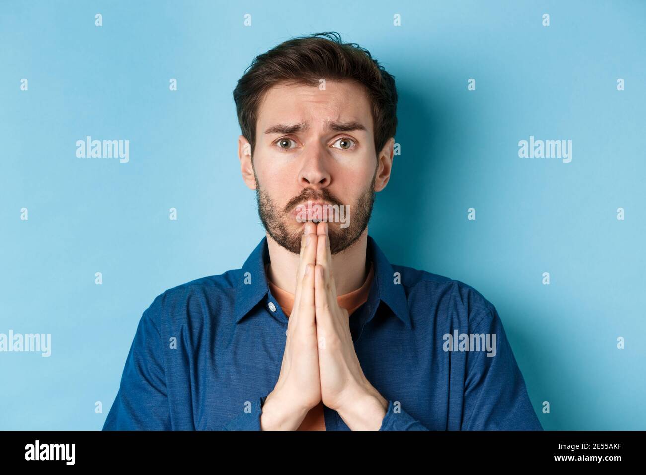 Sad young man begging for help, apoligizing and sobbing miserable, standing on blue background Stock Photo