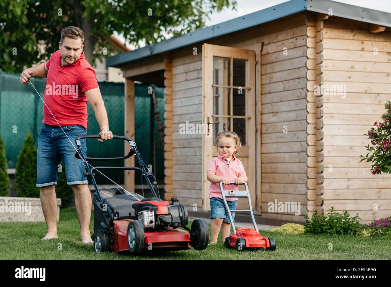 Father and his son mowing the lawn together. Full length of a young boy cutting the grass with