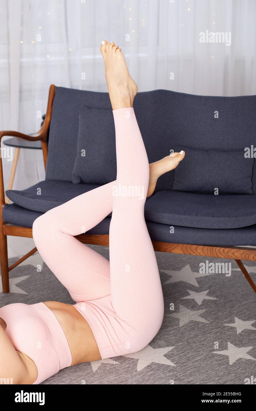 close-up the legs of a woman in pink sports leggings are raised on a gray soft sofa home interior Stock Photo