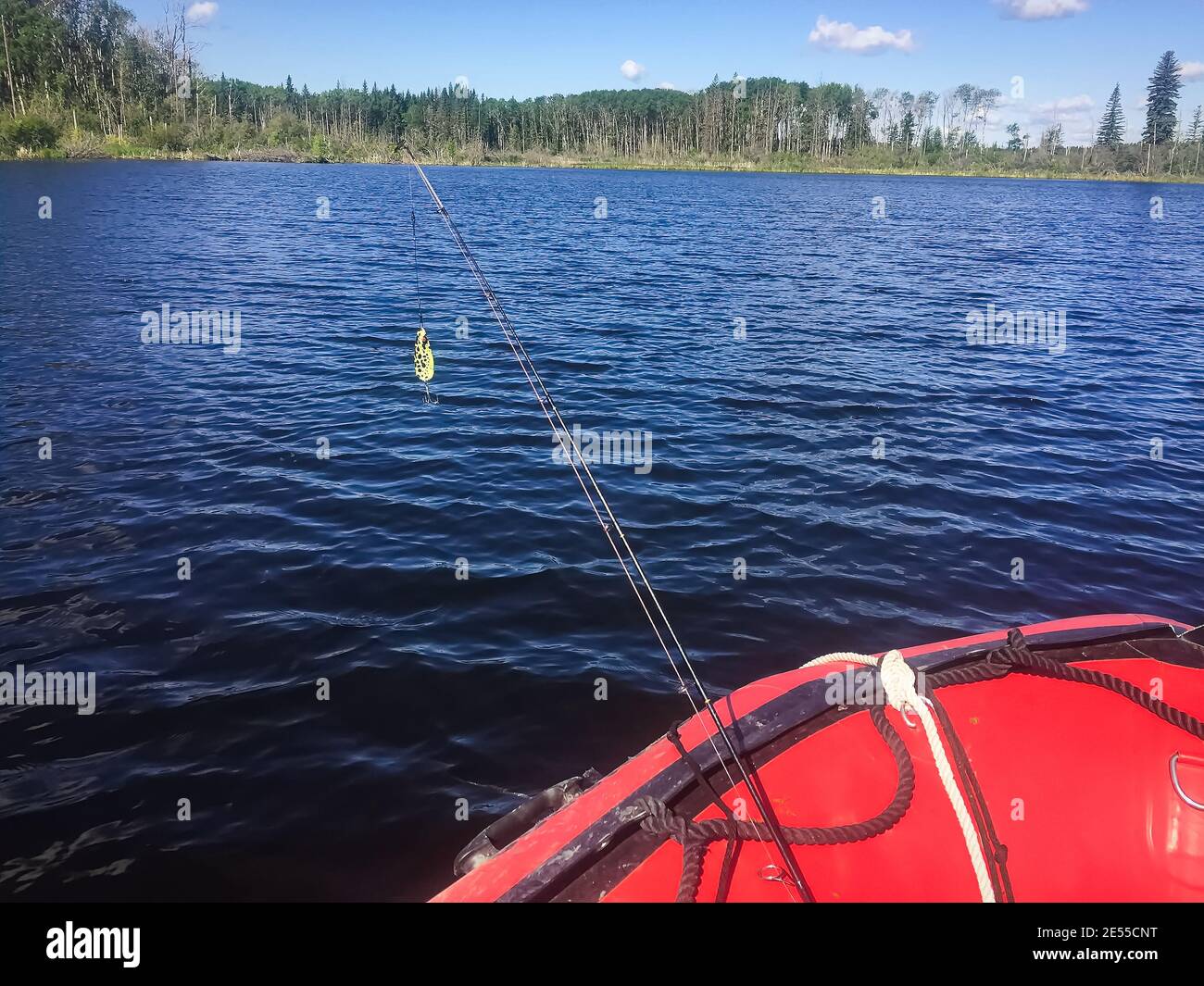 A fishing rod with hook over the edge of a boat in water Stock Photo