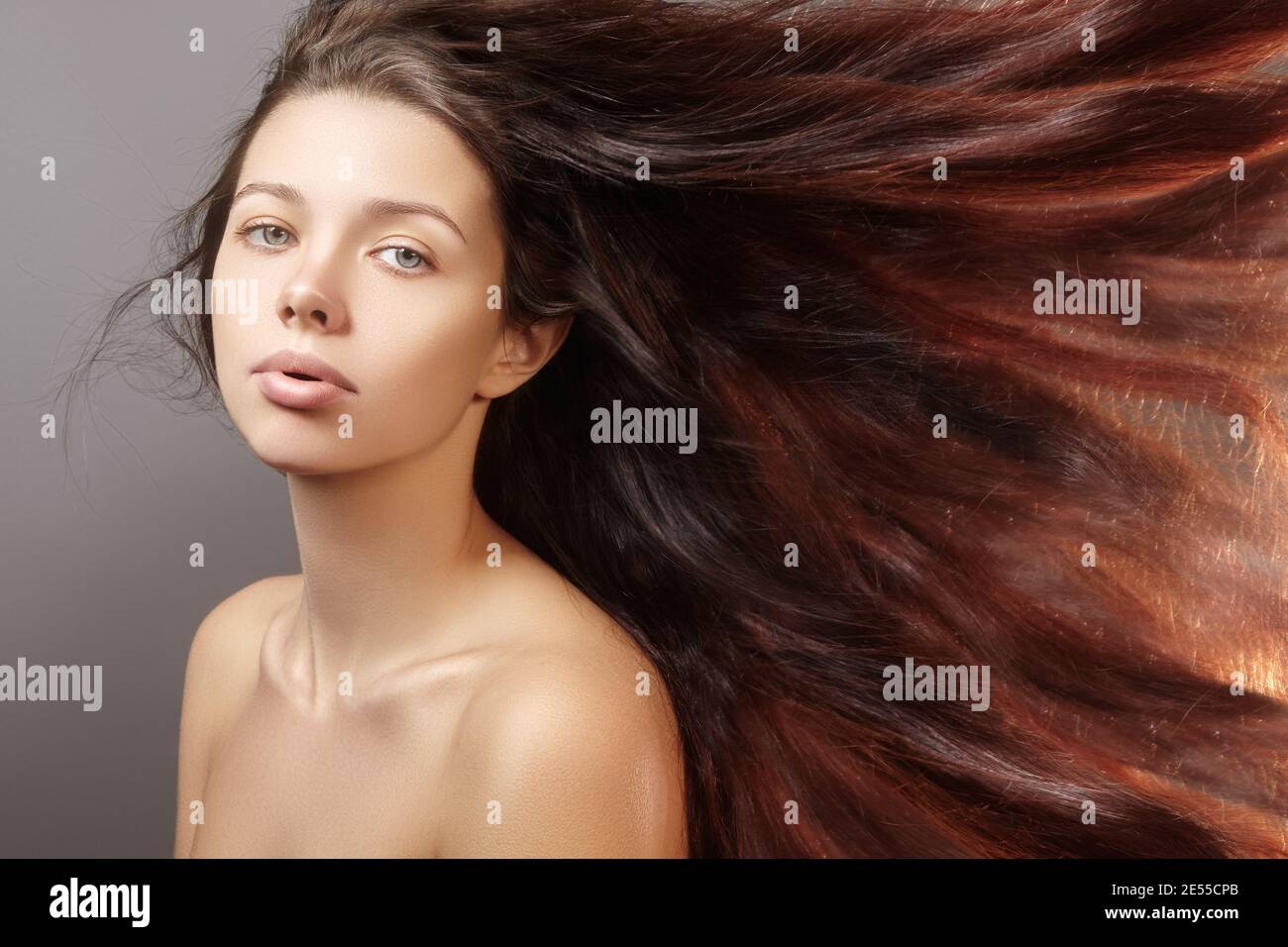 Brunette woman with hair fly up from the wind. Beautiful woman with clean skin and long brown hair. Close-up portrait on gray background Stock Photo