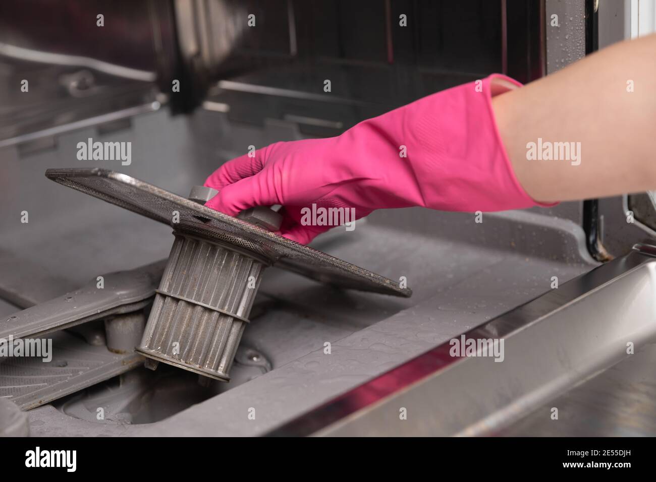 Women in rubber gloves showing a dirty dishwasher filter. Preparing for
