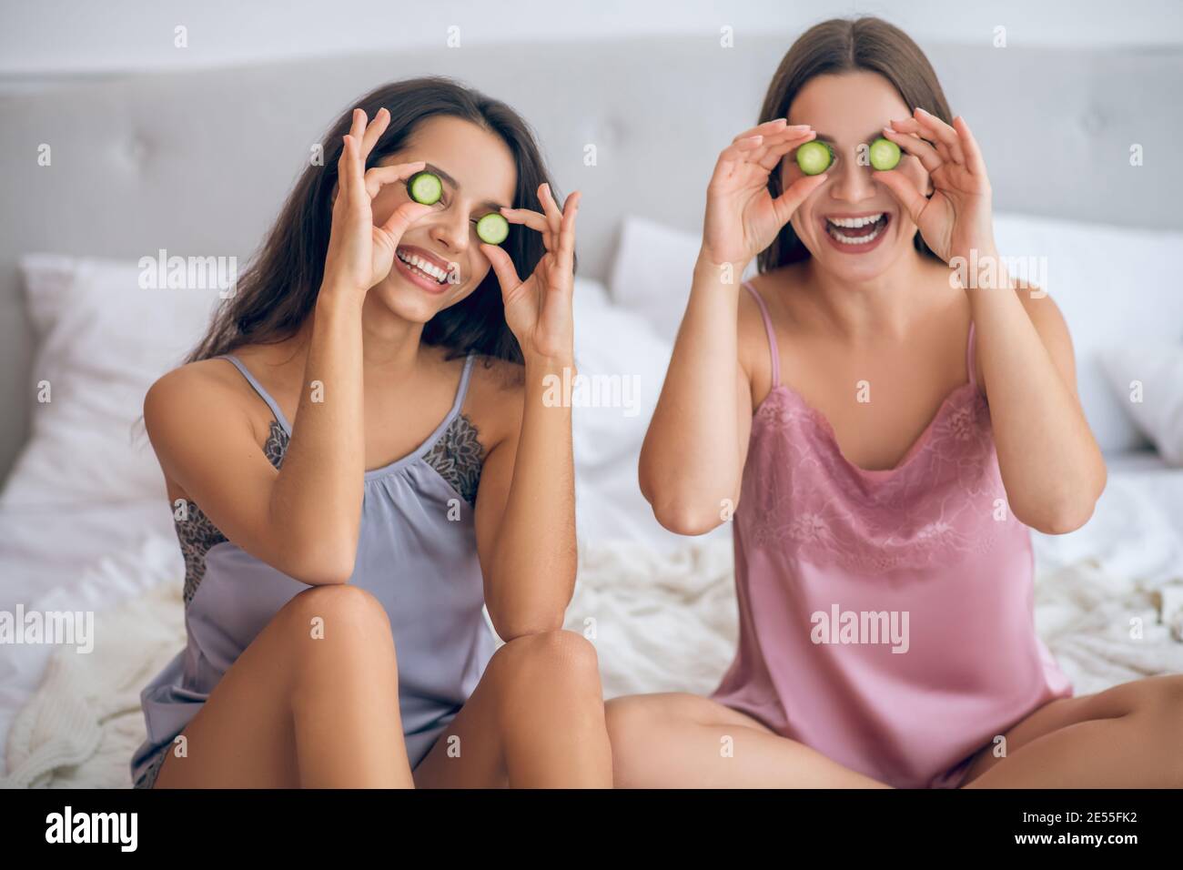 Two cute young girls with slices of cucumber in hands Stock Photo