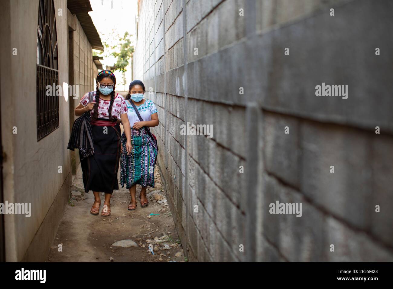 Young women walk in a narrow alley wearing protective facial masks in San Juan la Laguna, Guatemala, Central America. Stock Photo