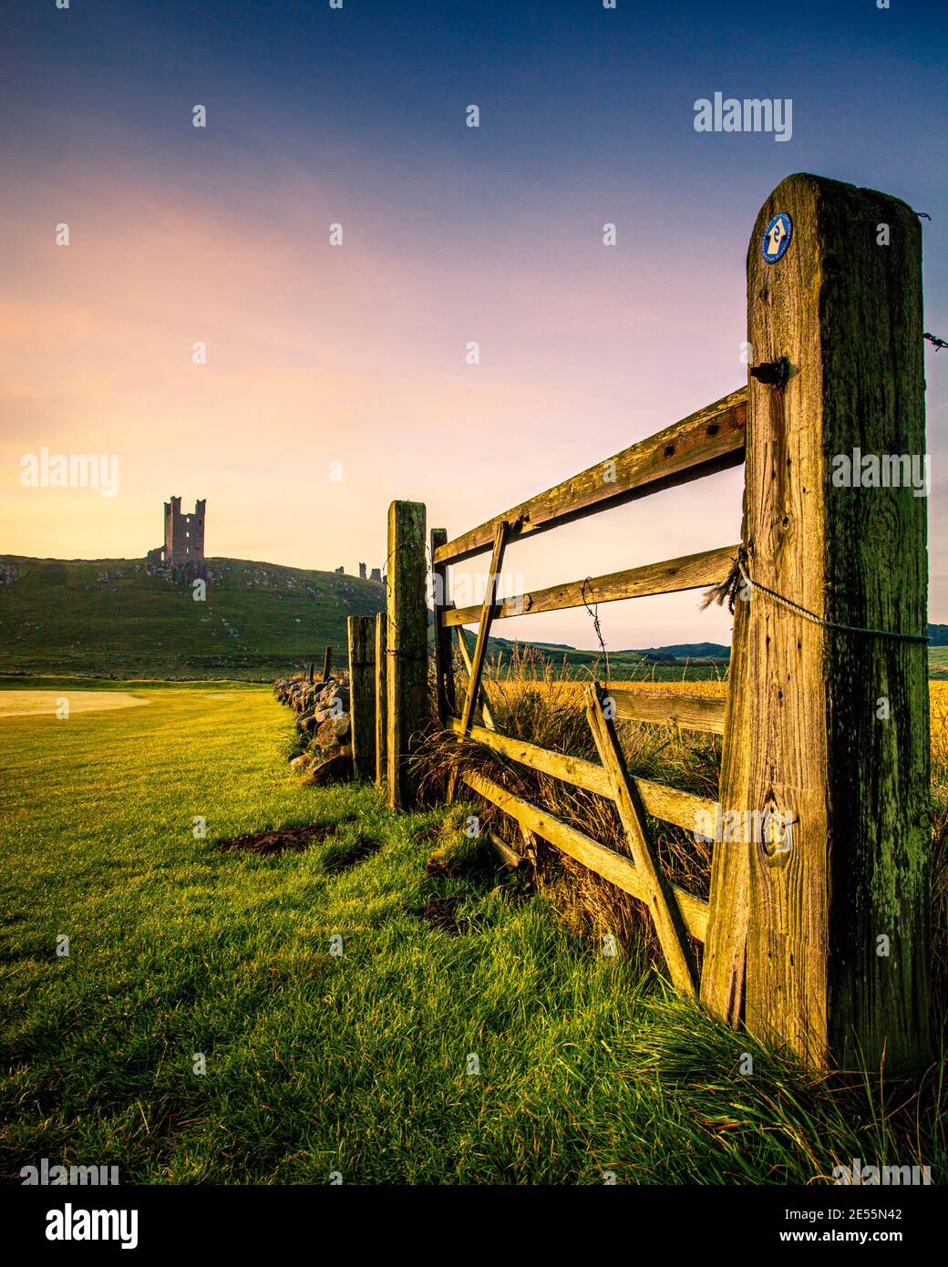 Dunstanburgh castle in Northumberland viewed through a field gate. Stock Photo