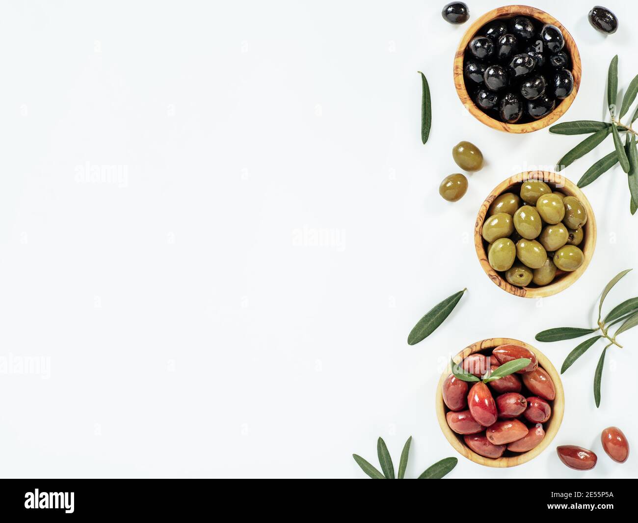Set of green olives, black olives and red kalmata olives on white background,copy space. Top view of different olives types in bowls and leaves and branches isolated on white. Beautiful olive flat lay Stock Photo