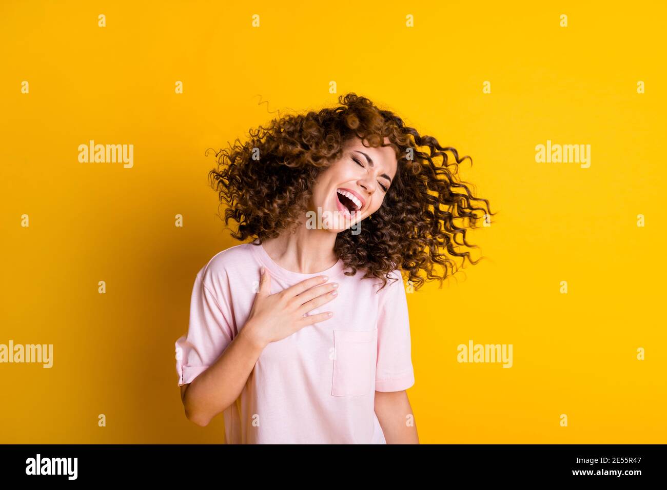 Photo portrait of woman laughing touching chest with one hand flying hair isolated on vivid yellow colored background Stock Photo