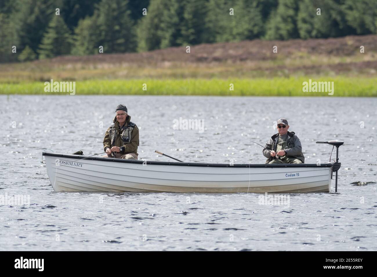 Two men (70s) fly-fishing for trout in a white boat on a Scottish moorland loch or lake Stock Photo