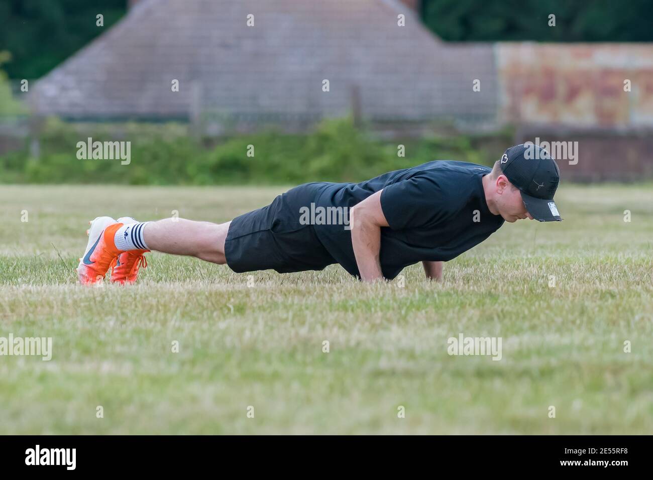 Young man (20s) planking on grass pitch, holding his body horizontal on his hands and toes. Stock Photo