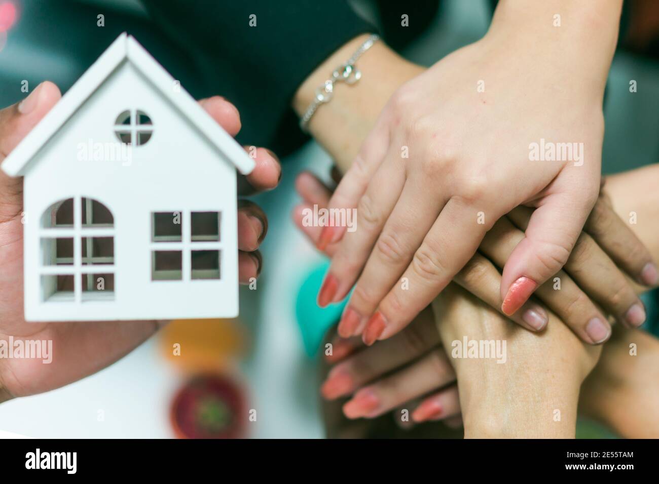 Young people putting their hands together. Friends with stack of hands showing unity and teamwork. Top view of hands and little white house. Real esta Stock Photo
