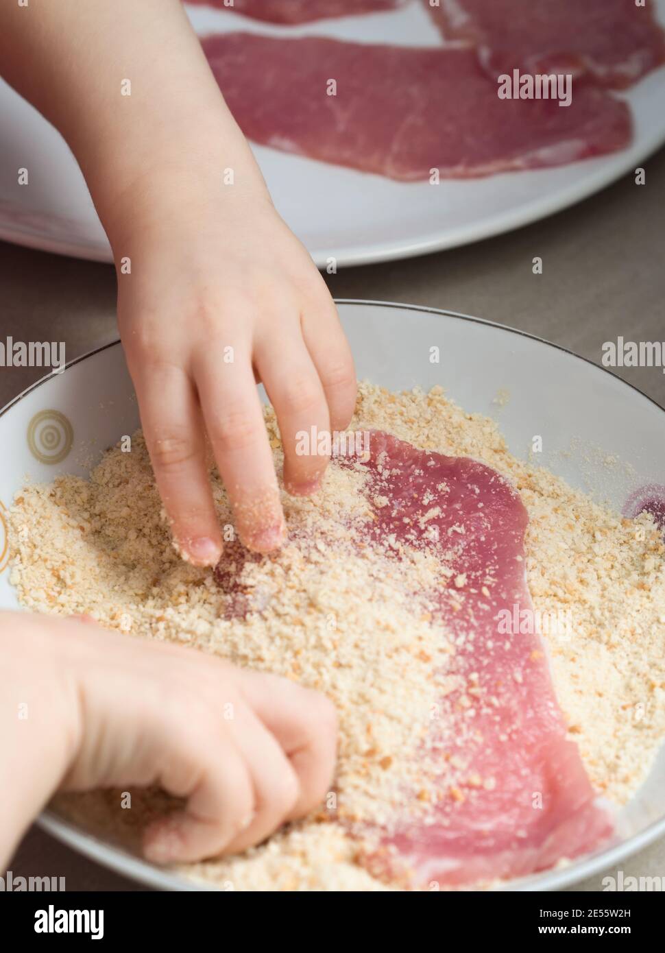 Child Covering Pork Meat with Breadcrumbs in the Kitchen Stock Photo