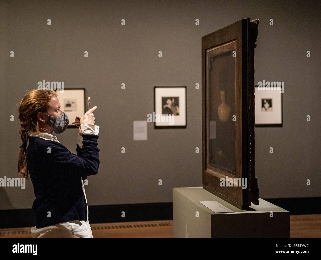A woman wearing face covering takes a photograph of a painting by Aubrey Beardsley mounted on a free standing double face frame. Stock Photo