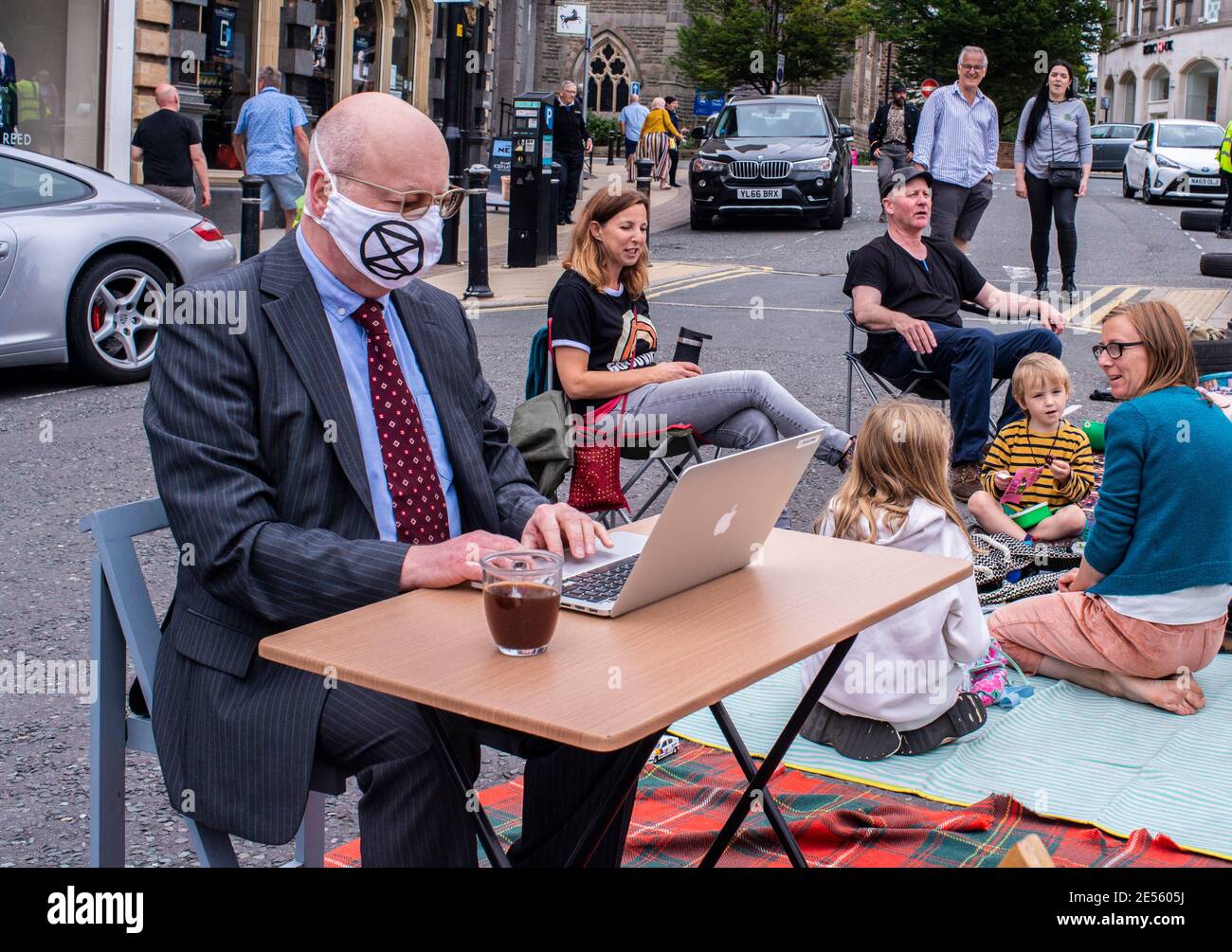 A member of Extinction Rebellion wearing a suit and a branded face mask takes part in a protest to reclaim public areas by putting up his own office in the middle of a parking area. Stock Photo