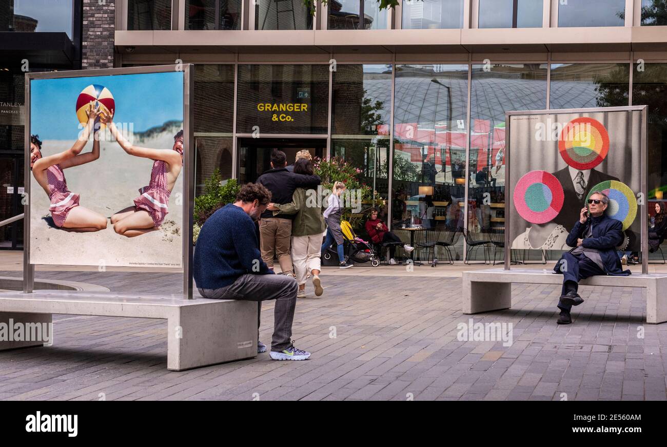People sitting on benches outside bar near Kings Cross with colourful pictures behind them. Stock Photo