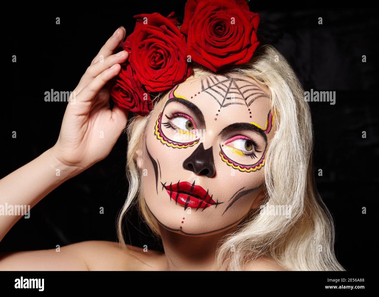Beautiful Halloween Make-Up Style. Blond Model Wear Sugar Skull Makeup with Red Roses, pale Skin Tones and Waves Hair. Santa Muerte concept Stock Photo